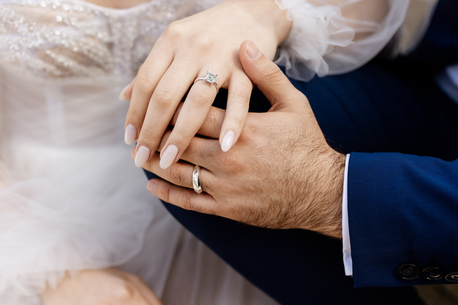 Close-up of hands holding each other with wedding rings, one person wearing a suit.