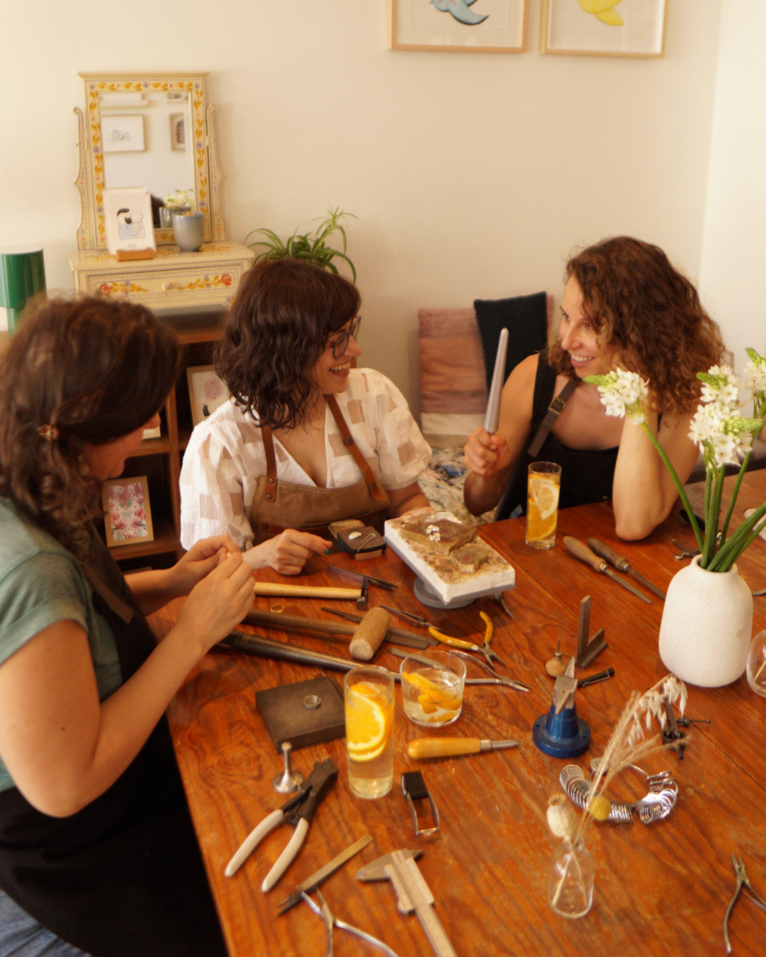 Three women sitting around a table with jewelry-making tools and materials.
