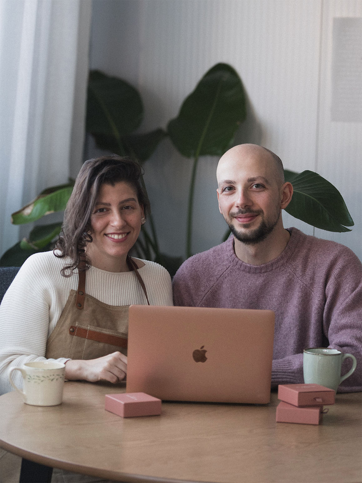 Two jewelers sitting at a table with a laptop, in Lisbon jewelry studio, smiling and looking at the camera.