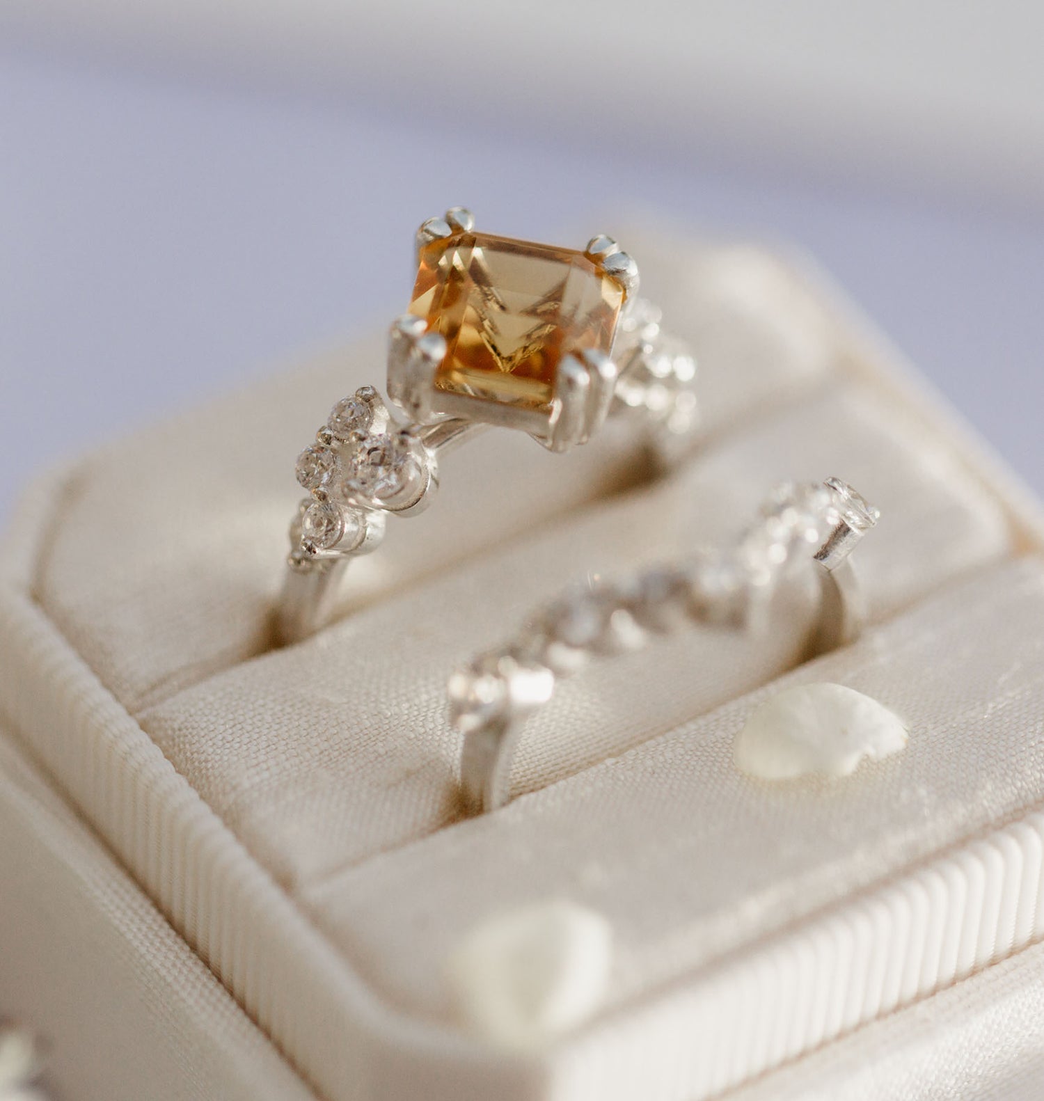 White gold ring with a large orange gemstone and smaller diamonds on a beige jewelry box.