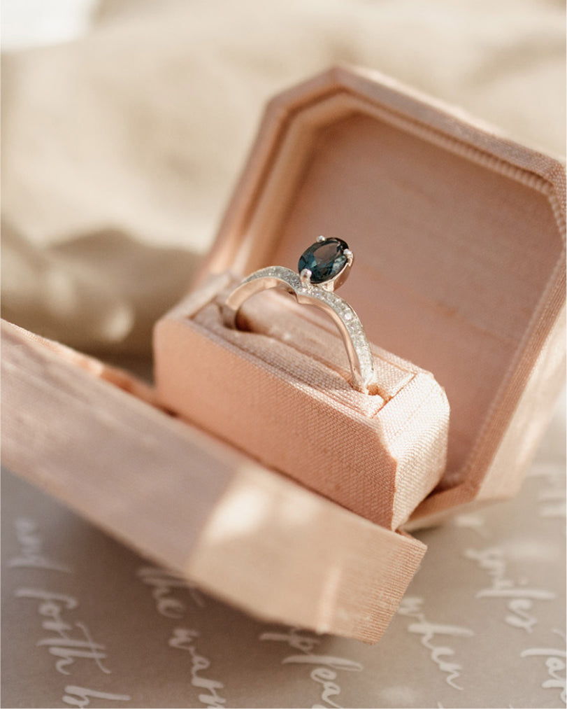 Ring with a london blue topaz stone in an open pink jewelry box on a textured surface in Lisbon.