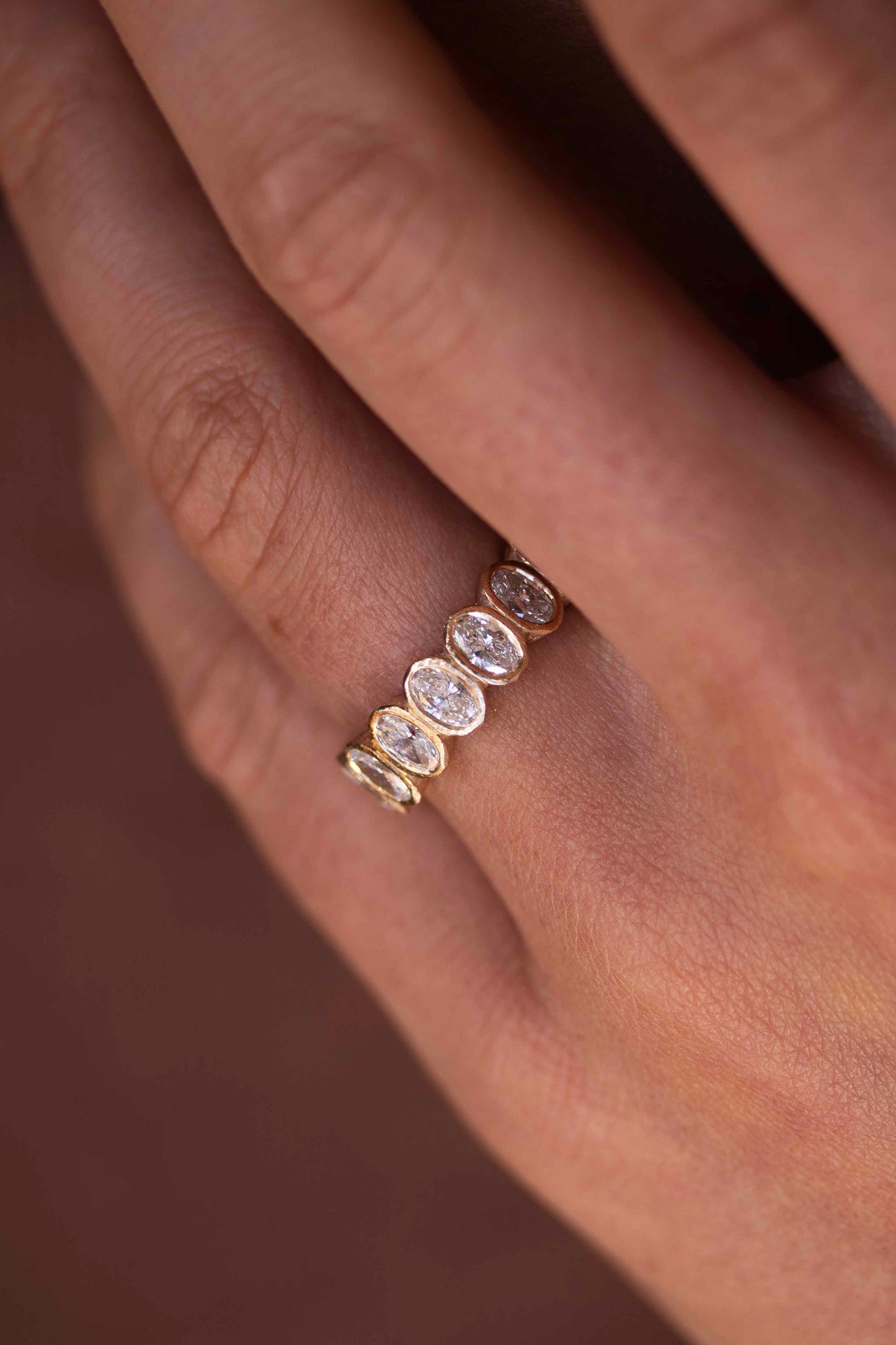 Close up of bezel set oval diamond eternity ring on finger by Amaré