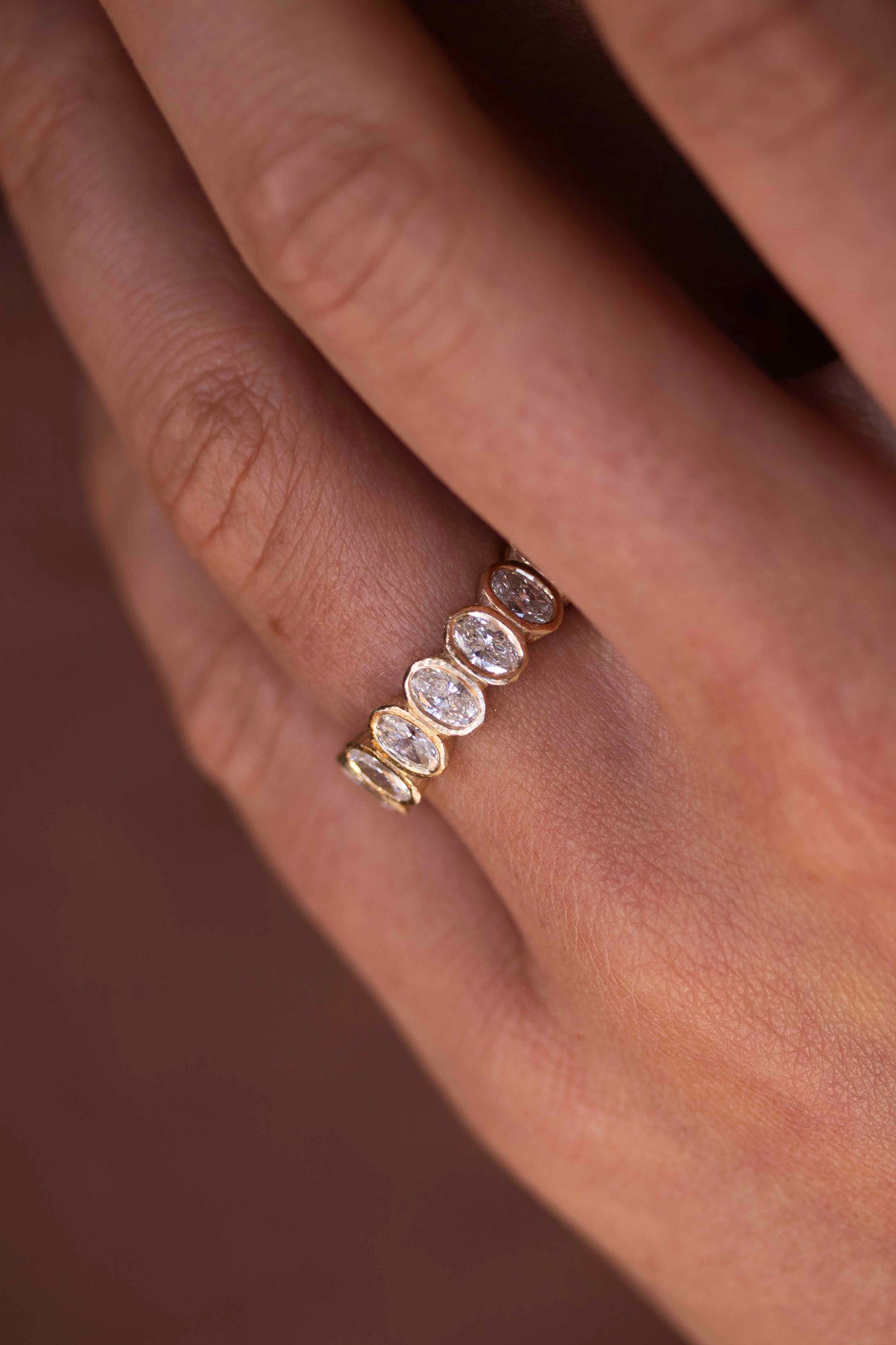 Close up of bezel set oval diamond eternity ring on finger by Amaré