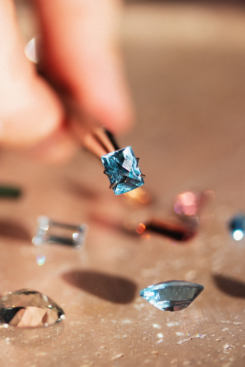 Close-up of a diamond being held by tweezers with other diamonds on a reflective surface.