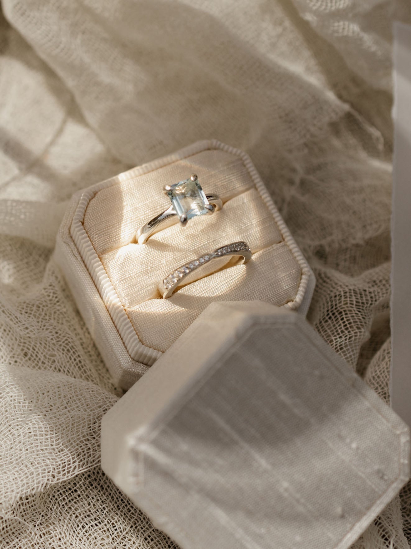 Open jewelry box with two diamond rings on a textured fabric background